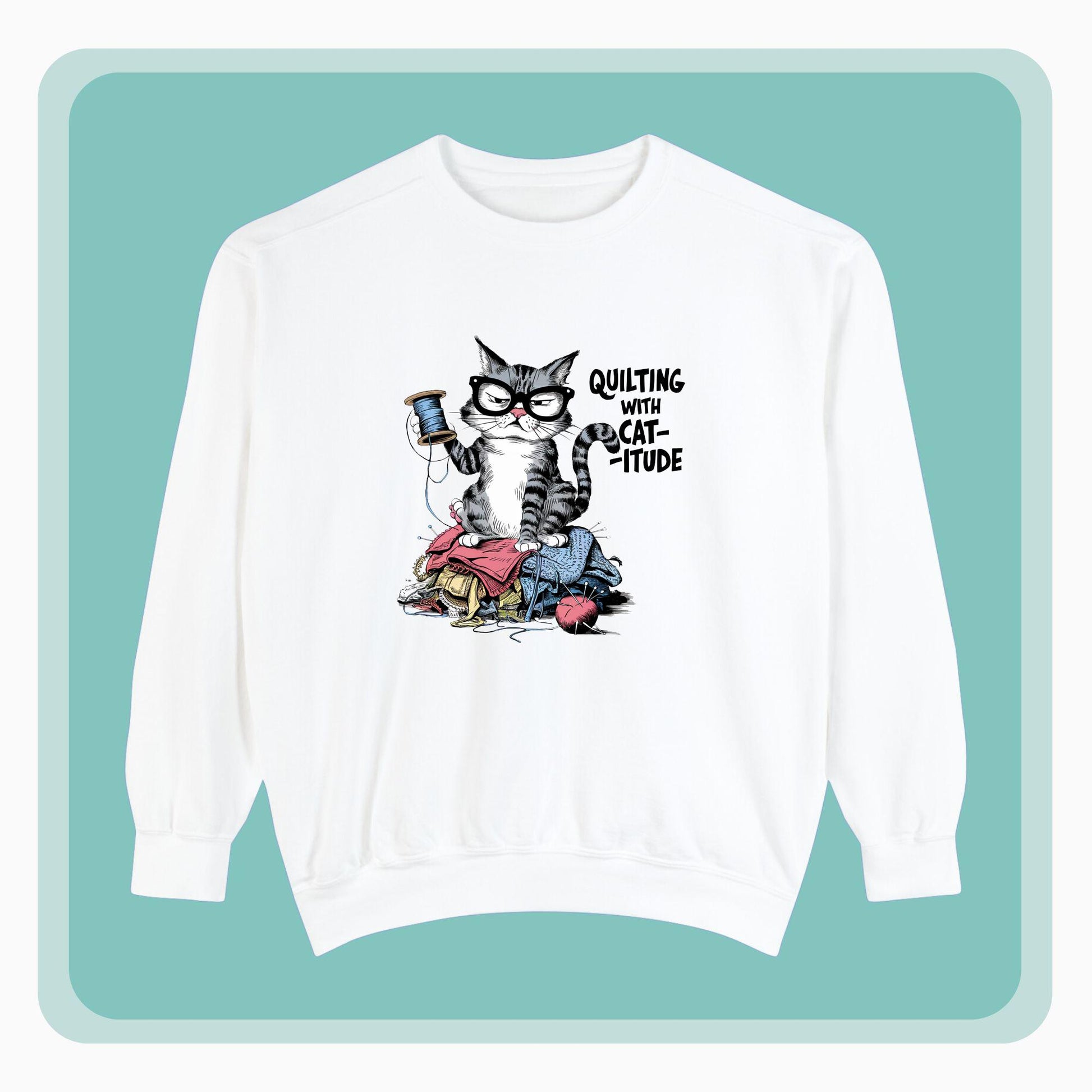 A sweatshirt featuring a sassy cartoon cat sitting on a pile of colorful fabric, holding a spool of thread, with the phrase 'Quilting with Cat-itude,' perfect for quilters and cat lovers.