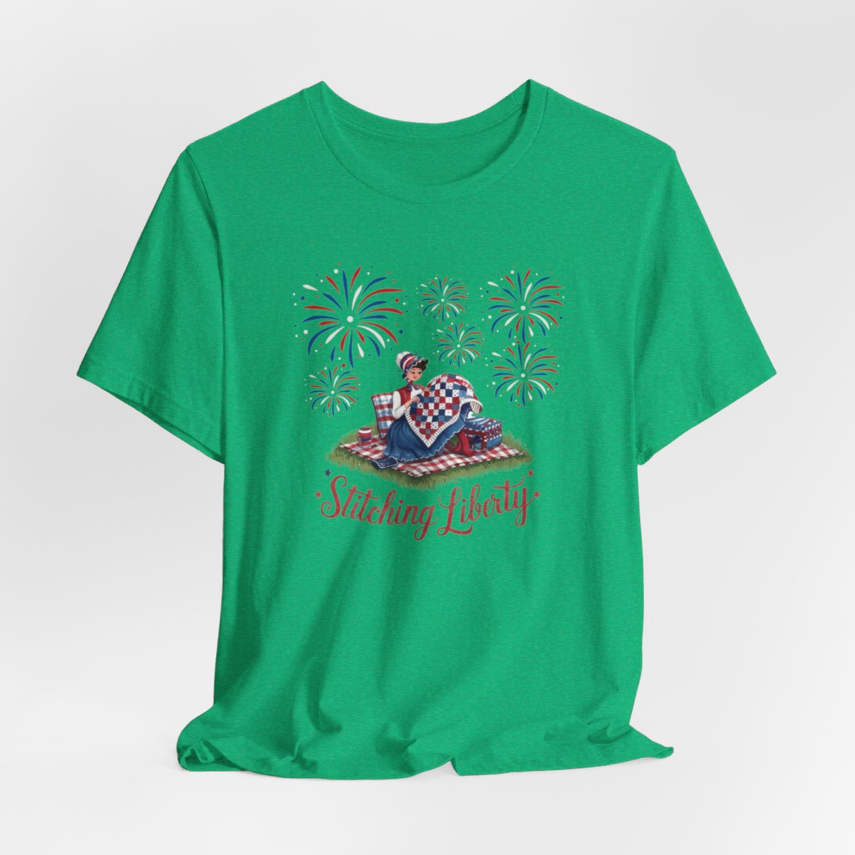 A Heather Kelly T-shirt with illustrated scene of a colonial woman quilting a patriotic blanket, surrounded by fireworks. Text reads "Stitching Liberty" in a decorative font.