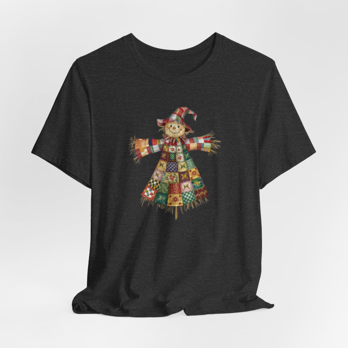 A Dark Grey Heather thanksgiving  quilting t-shirt featuring a smiling scarecrow made entirely of colorful quilt patterns. Wearing a patchwork hat and clothes with various quilt designs. Straw details on hands and neck. Cheerful autumn-themed illustration celebrating quilting craft.