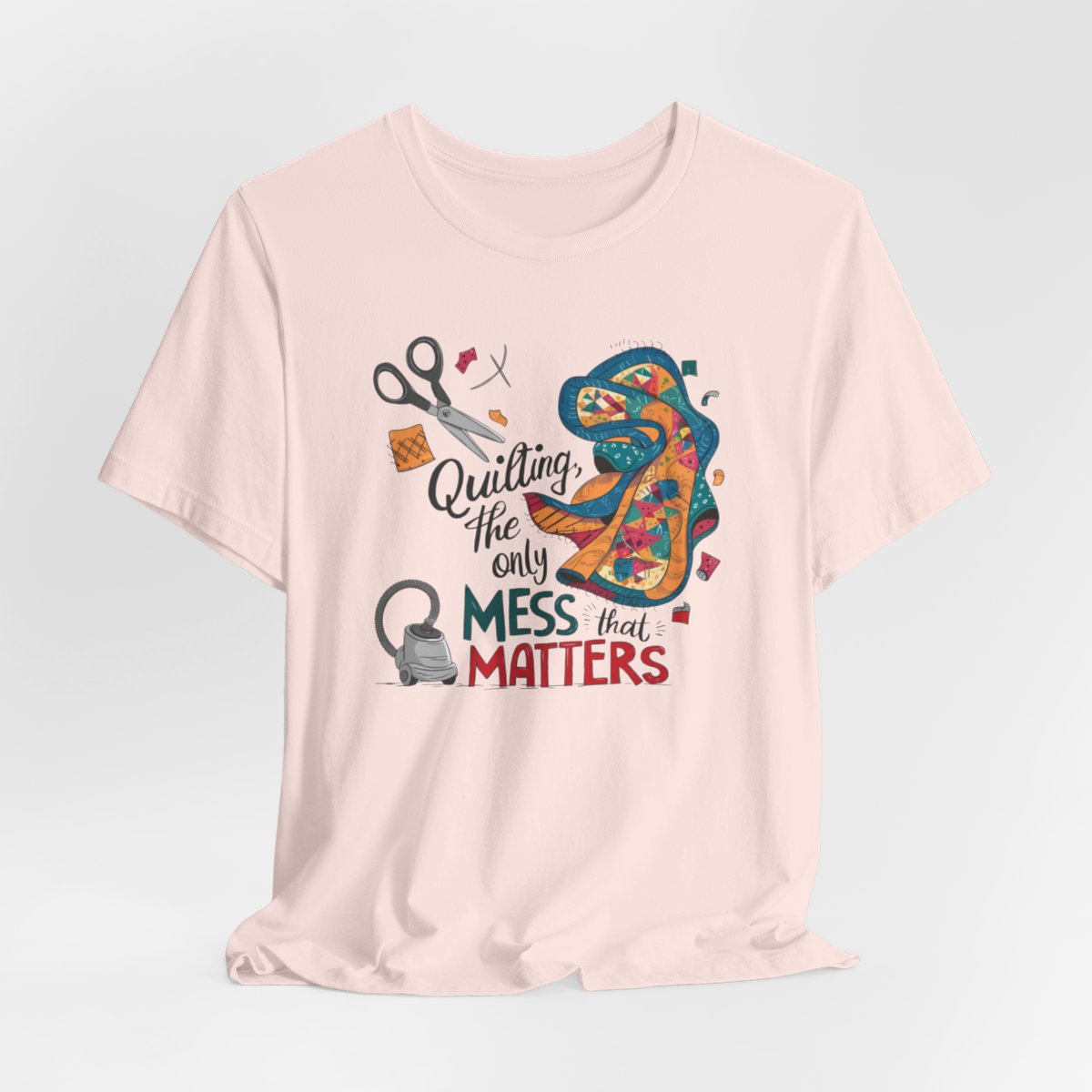 A Soft Pink fun T-Shirt with the phrase Quilting, the Only Mess that Matters and illustrations of fabric scraps, scissors, and a vacuum cleaner. Colorful quilt patterns swirl around the text, creating a playful and relatable design for quilting enthusiasts.