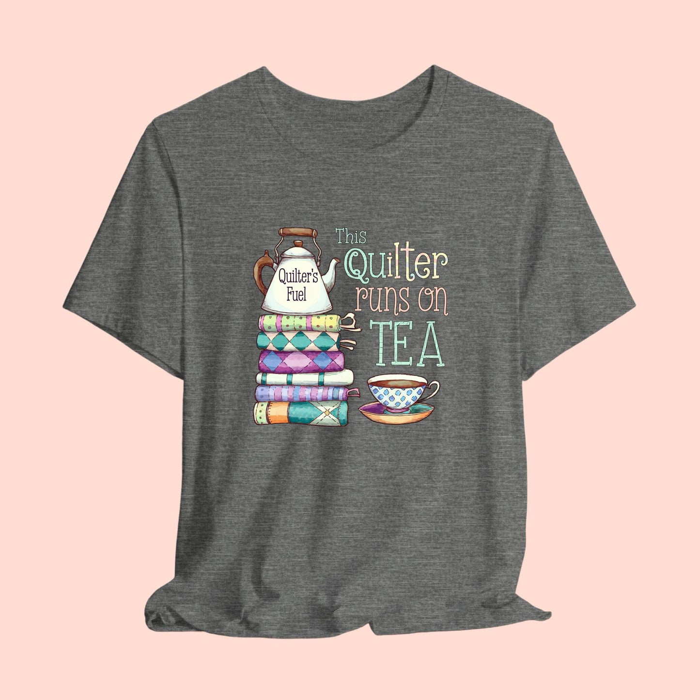 A t-shirt featuring a whimsical design of a stack of patchwork quilts with a teapot labeled 'Quilter's Fuel' and the phrase 'This Quilter Runs on Tea,' ideal for tea-loving quilters.