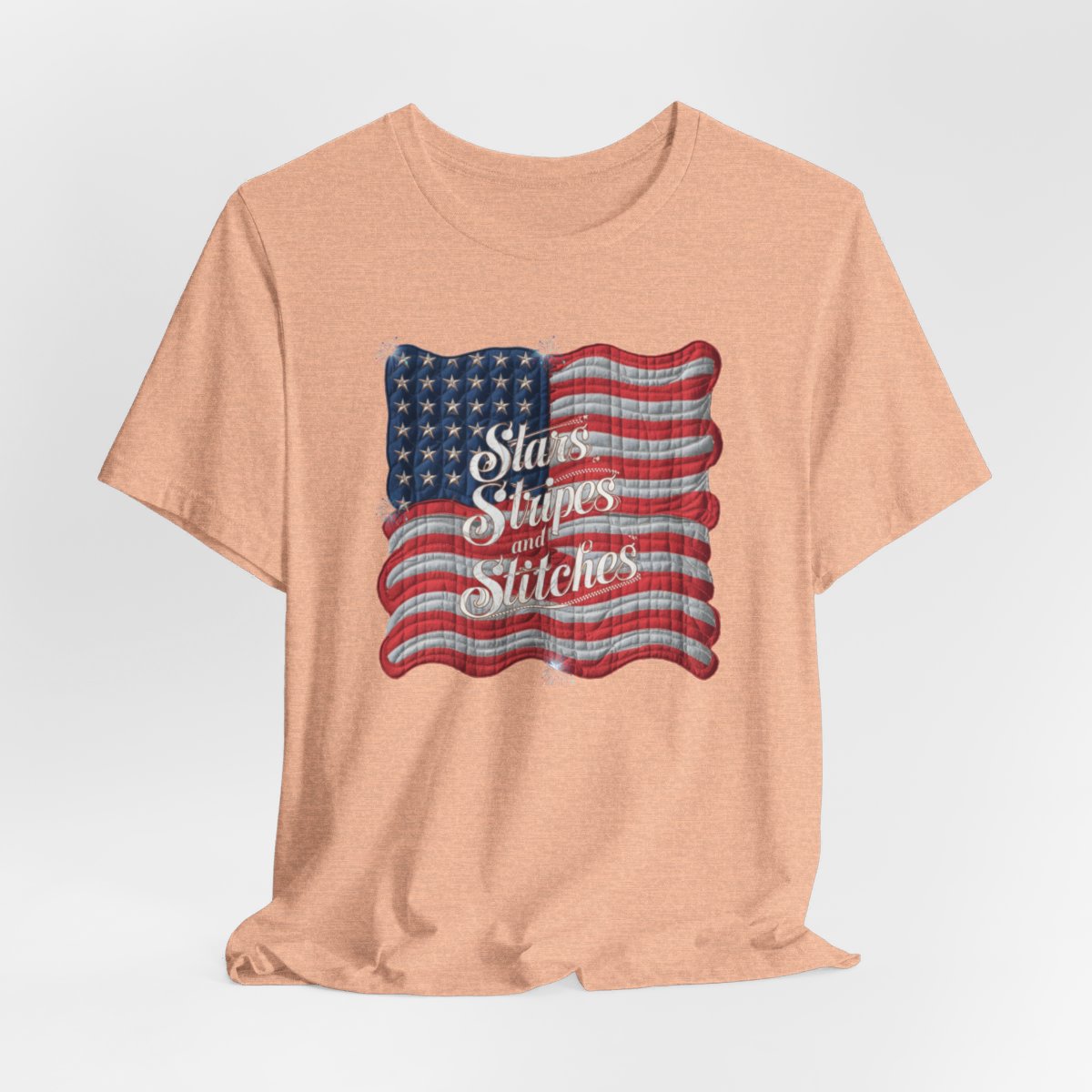 A Heather Peach T-shirt featuring quilted American flag design with text "Stars Stripes and Stitches" overlaid in stylized, patriotic font. Fireworks accent the corners.