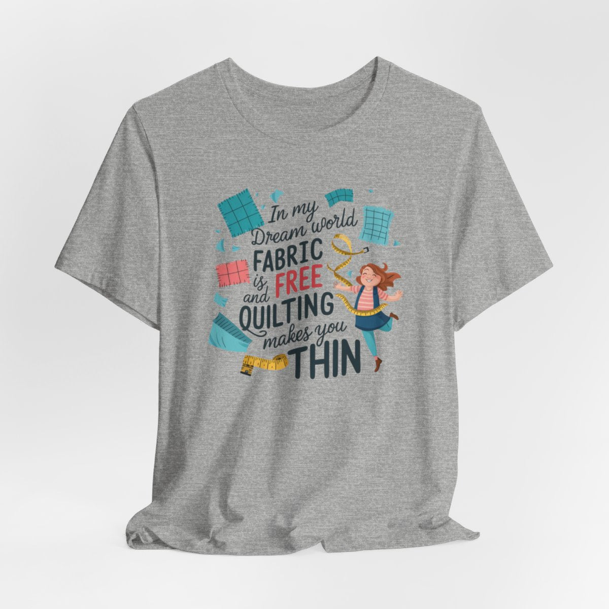 An Athletic Heather funny quilting T-Shirt with the phrase Fabric is Free and Quilting Makes You Thin in a fun font with a cheerful quilter jumping for joy