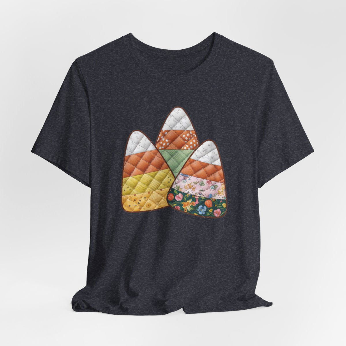 A Heather Navy Halloween Quilting T-Shirt featuring three large candy corn shapes made of quilted fabrics with various patterns. Each candy corn section features different quilting motifs in autumn colors. Playful take on Halloween candy and quilting craft.