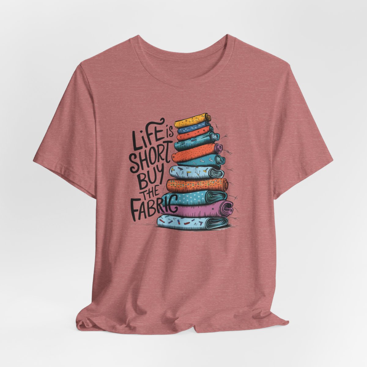 A Heather Mauve fun T-Shirt with the phrase Life is Short, Buy the Fabric with the label 'Life is Short, Buy the Fabric' next to a graphic of a fun pile of fabric