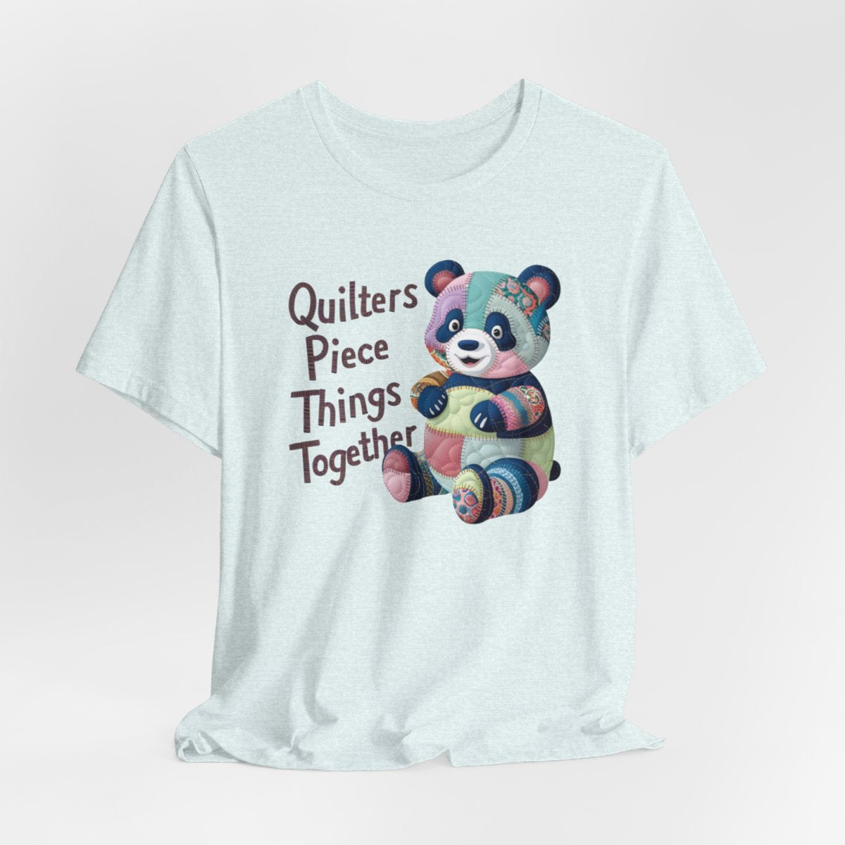 A Heather Ice Blue fun T-Shirt with the phrase Quilters Piece Things Together with a patchwork panda design . The panda is made of colorful fabric scraps stitched together, creating a whimsical and crafty appearance. Perfect for quilting enthusiasts with a sense of humor.