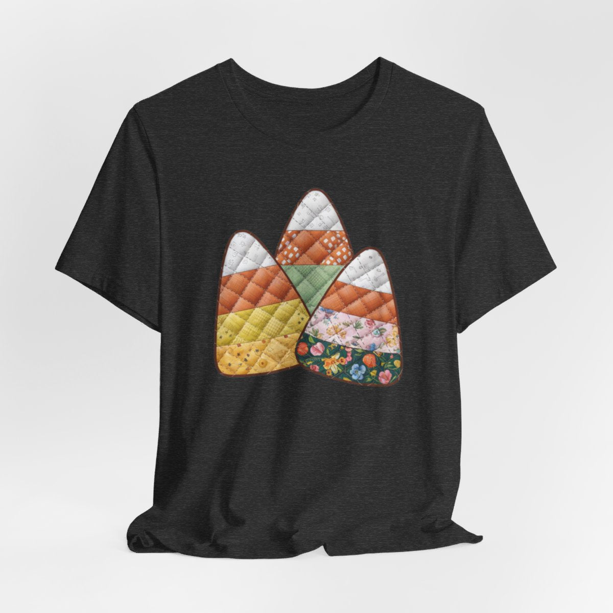 A Dark Grey Heather Halloween Quilting T-Shirt featuring three large candy corn shapes made of quilted fabrics with various patterns. Each candy corn section features different quilting motifs in autumn colors. Playful take on Halloween candy and quilting craft.