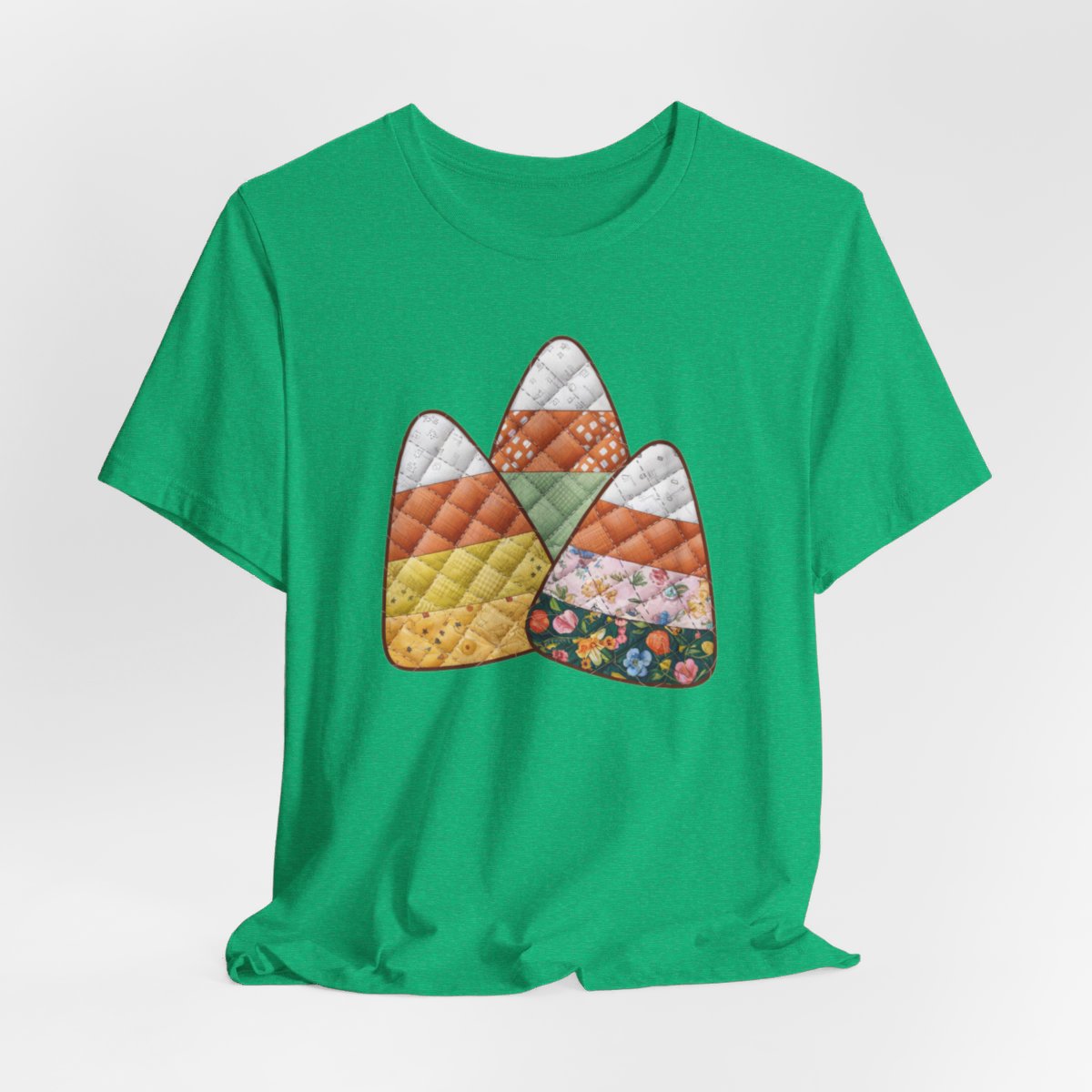 A Heather Kelly Halloween Quilting T-Shirt featuring three large candy corn shapes made of quilted fabrics with various patterns. Each candy corn section features different quilting motifs in autumn colors. Playful take on Halloween candy and quilting craft.