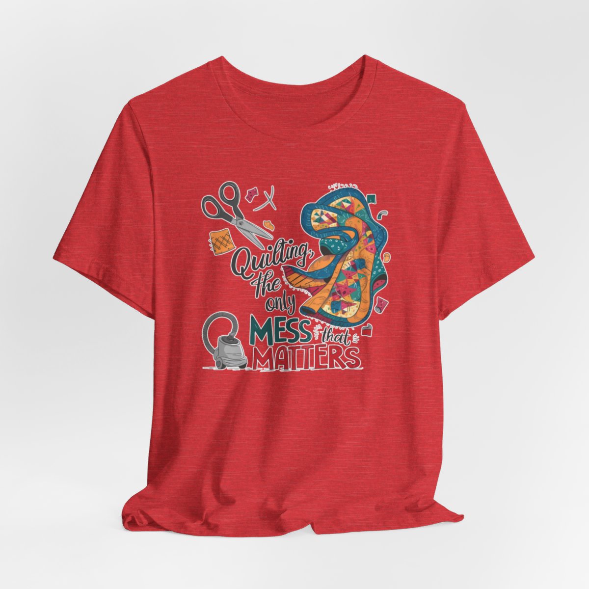 A Heather Red fun T-Shirt with the phrase Quilting, the Only Mess that Matters and illustrations of fabric scraps, scissors, and a vacuum cleaner. Colorful quilt patterns swirl around the text, creating a playful and relatable design for quilting enthusiasts.