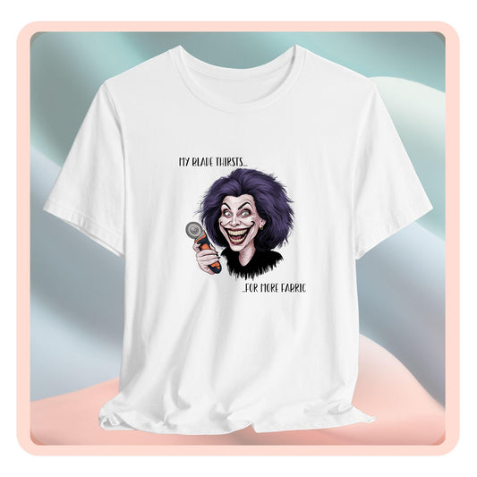 A T-shirt showing a cartoonish character with wild purple hair and an exaggerated grin, holding a rotary cutter. Text reads "My blade thirsts... for more fabric", humorously depicting a quilter's endless desire for new materials.