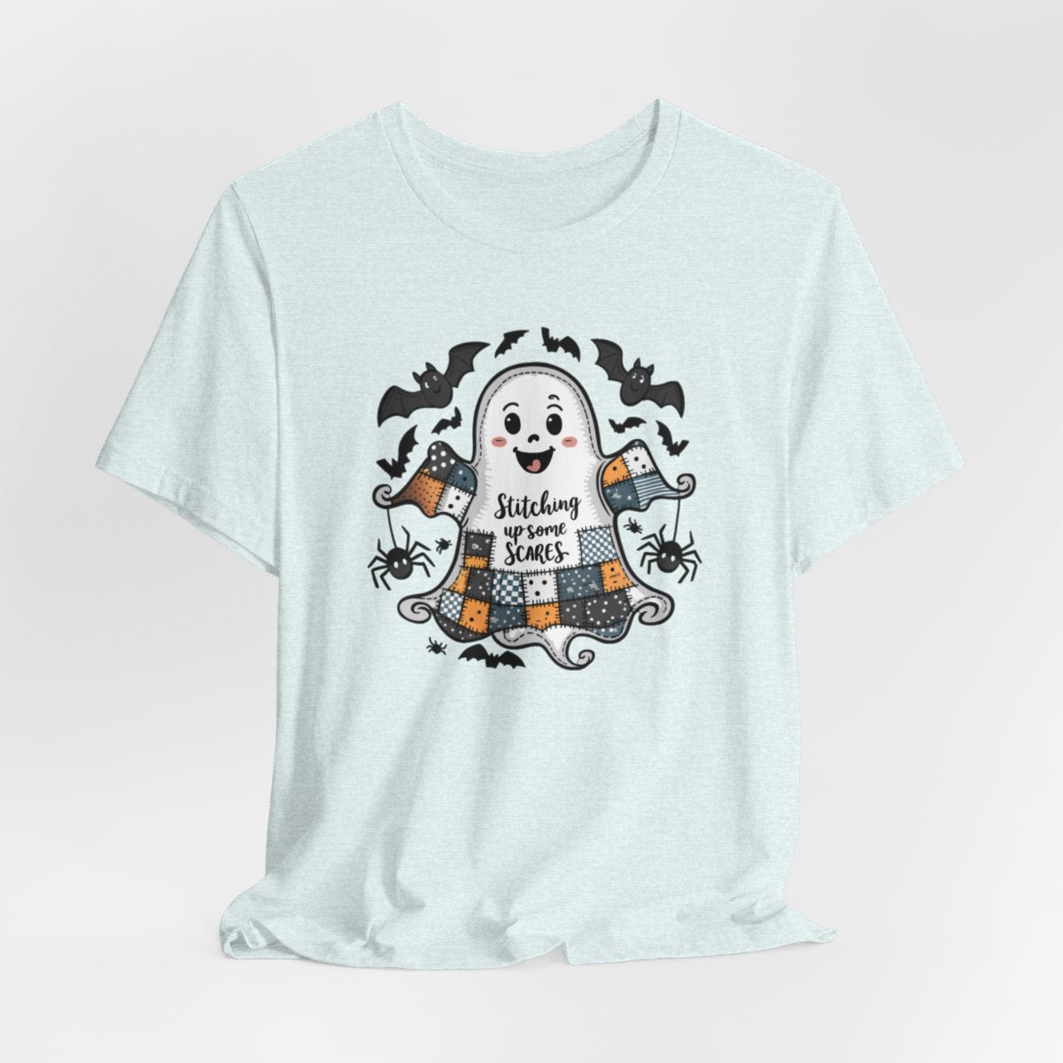 A Heather Ice Blue Halloween Quilting T-Shirt featuring a smiling ghost with quilted patchwork body. Halloween-themed quilt patterns. Cute bats and spiders around ghost. Text reads "Stitching up some Scares". Ideal for quilters who enjoy Halloween themes.