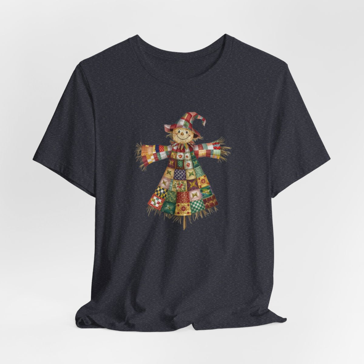 A Heather Navy thanksgiving  quilting t-shirt featuring a smiling scarecrow made entirely of colorful quilt patterns. Wearing a patchwork hat and clothes with various quilt designs. Straw details on hands and neck. Cheerful autumn-themed illustration celebrating quilting craft.