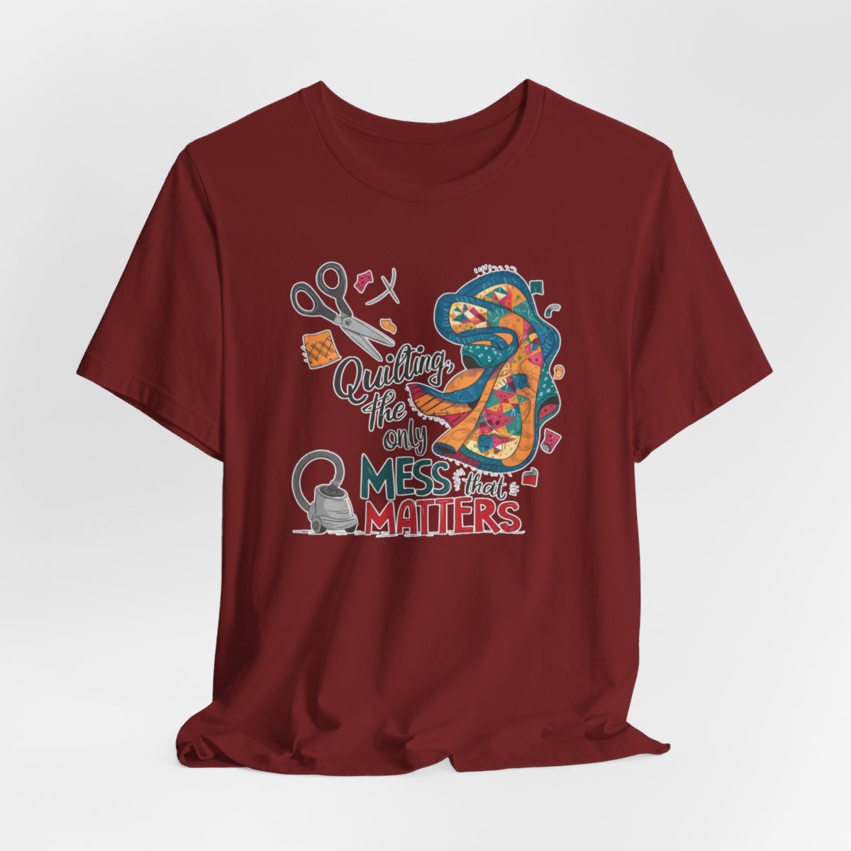 A Cardinal fun T-Shirt with the phrase Quilting, the Only Mess that Matters and illustrations of fabric scraps, scissors, and a vacuum cleaner. Colorful quilt patterns swirl around the text, creating a playful and relatable design for quilting enthusiasts.