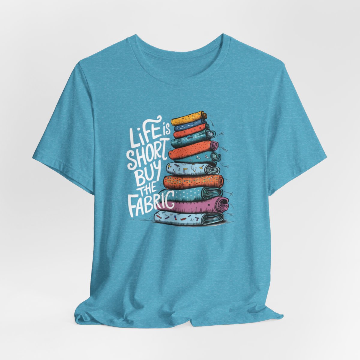 A Heather Aqua fun T-Shirt with the phrase Life is Short, Buy the Fabric with the label 'Life is Short, Buy the Fabric' next to a graphic of a fun pile of fabric