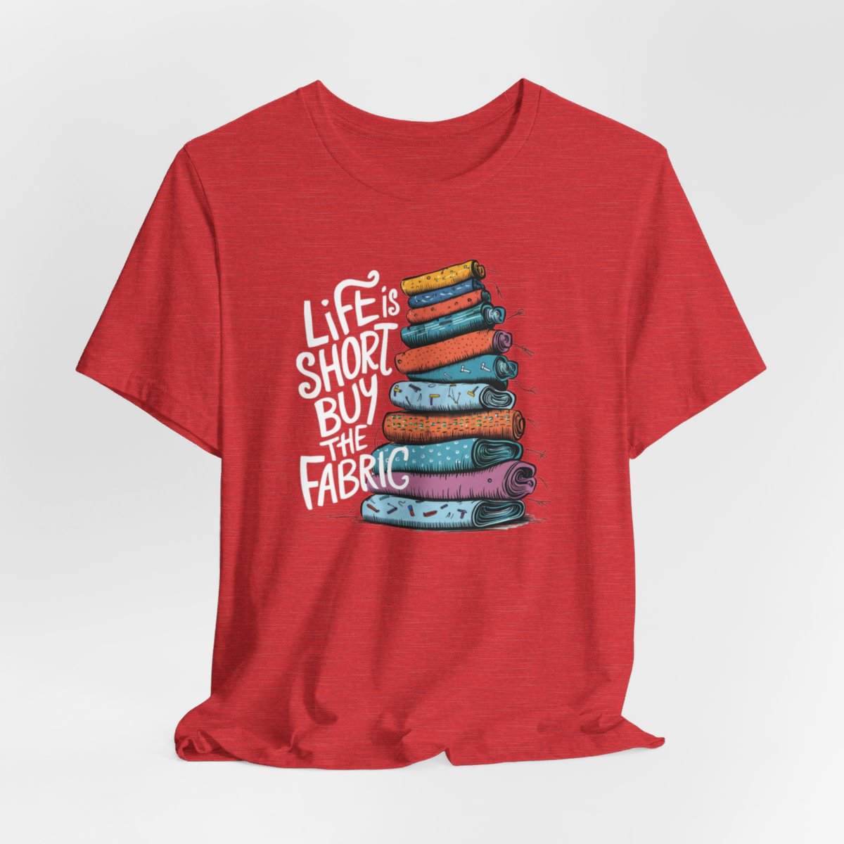 A Heather Red fun T-Shirt with the phrase Life is Short, Buy the Fabric with the label 'Life is Short, Buy the Fabric' next to a graphic of a fun pile of fabric