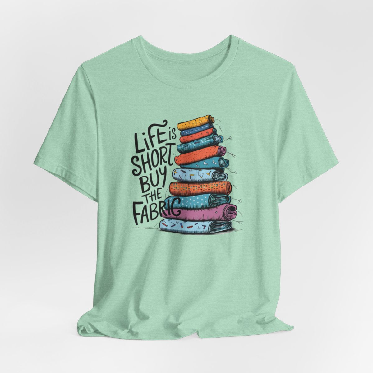 A Heather Mint fun T-Shirt with the phrase Life is Short, Buy the Fabric with the label 'Life is Short, Buy the Fabric' next to a graphic of a fun pile of fabric