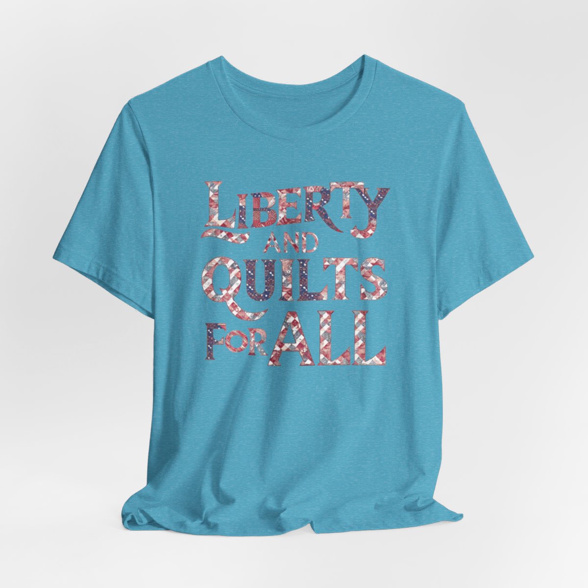 A Heather Aqua T-shirt featuring text "LIBERTY AND QUILTS FOR ALL" in large decorative letters filled with various quilt patterns in red, white, and blue.