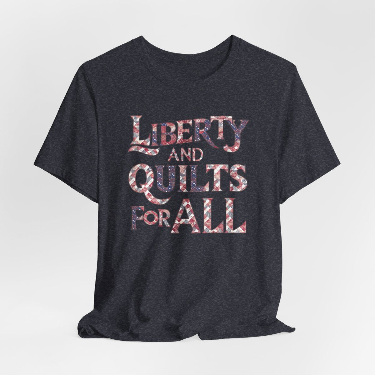 A Heather Navy T-shirt featuring text "LIBERTY AND QUILTS FOR ALL" in large decorative letters filled with various quilt patterns in red, white, and blue.