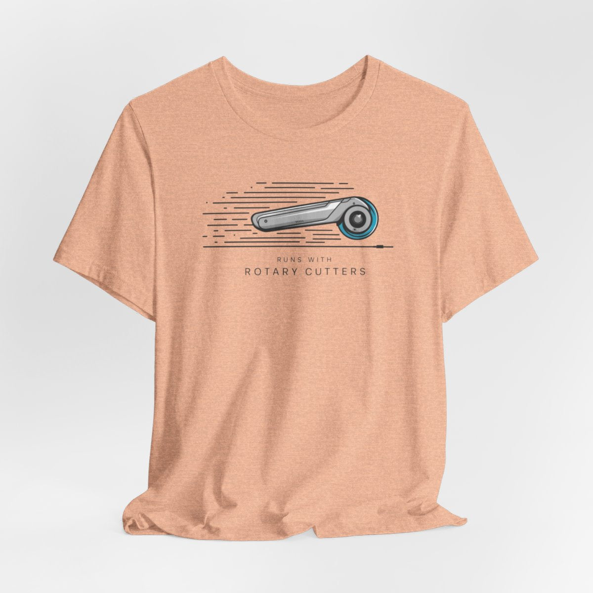 A Heather Peach T-shirt featuring minimalist graphic of a sleek rotary cutter in motion with speed lines. Text below reads "RUNS WITH ROTARY CUTTERS" in a modern font.