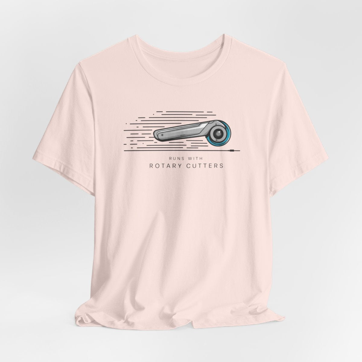 A Soft Pink T-shirt featuring minimalist graphic of a sleek rotary cutter in motion with speed lines. Text below reads "RUNS WITH ROTARY CUTTERS" in a modern font.